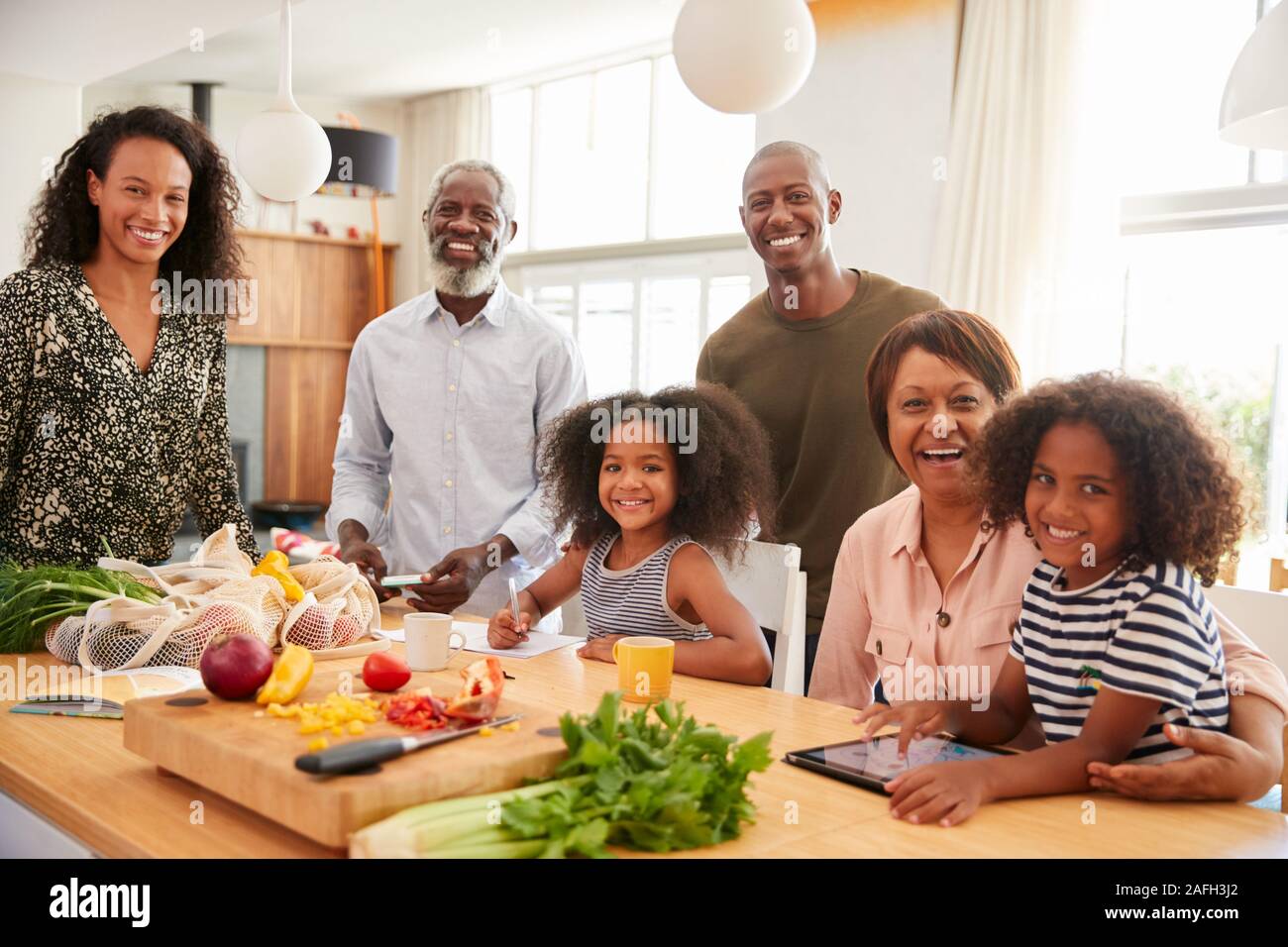 Portrait von Großeltern am Tisch sitzen mit Enkelkindern Spielen als Familie bereitet Essen Stockfoto