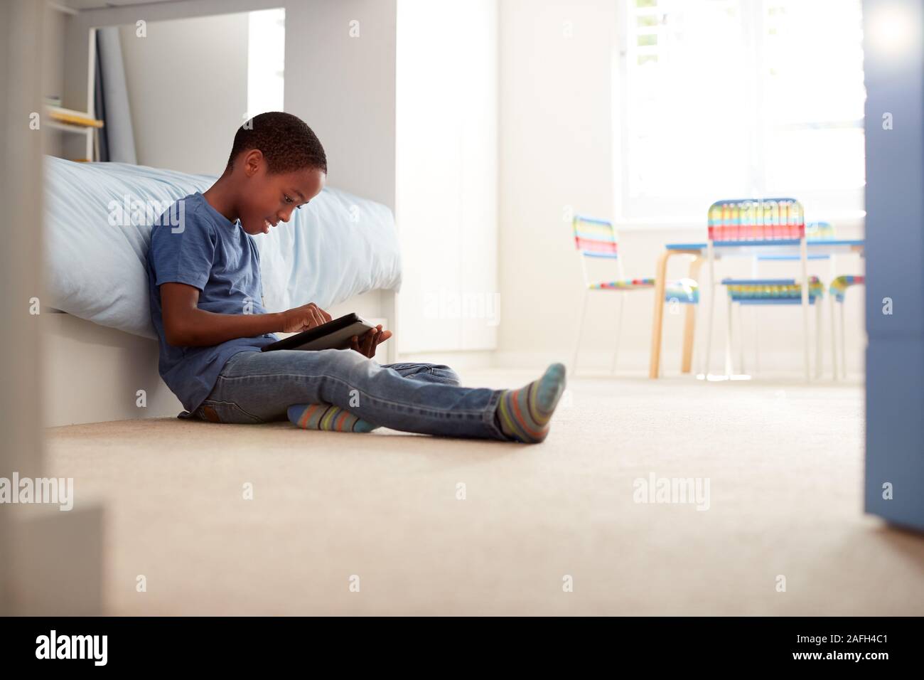 Junge sitzt auf dem Boden im Schlafzimmer mit digitalen Tablet Stockfoto