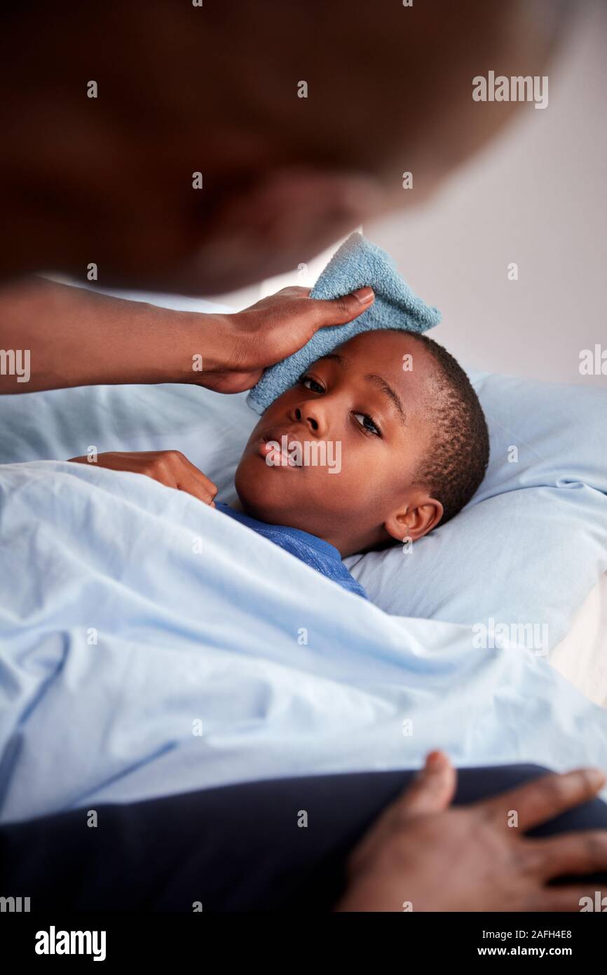 Vater die Sorge für die Kranken Sohn krank im Bett mit Temperatur Stockfoto