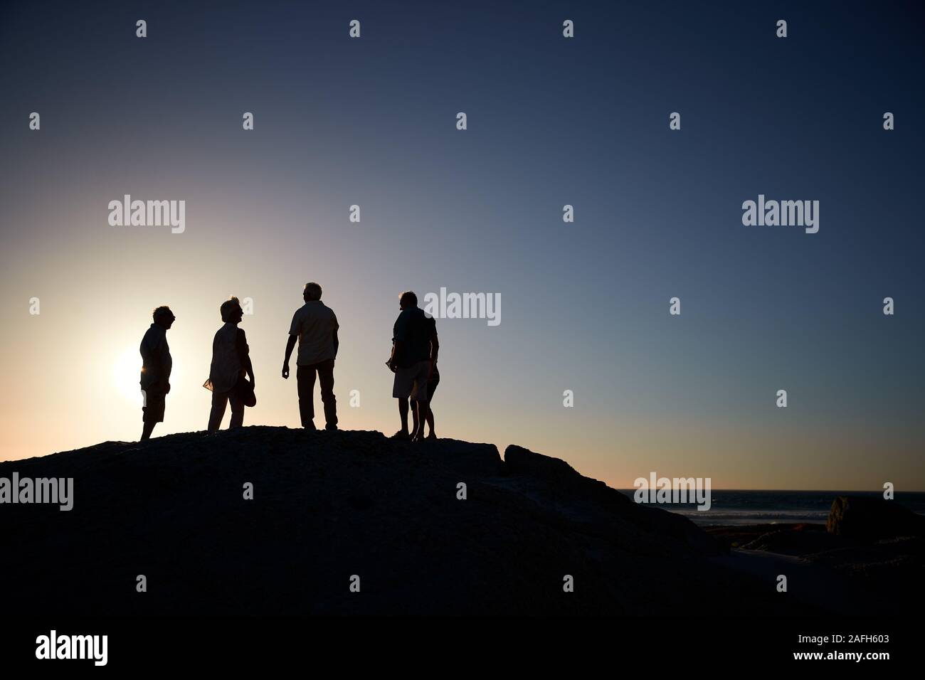 Silhouette der älteren Freunde stehen auf Felsen auf dem Seeweg durch Vermietungen bei Sonnenuntergang Stockfoto