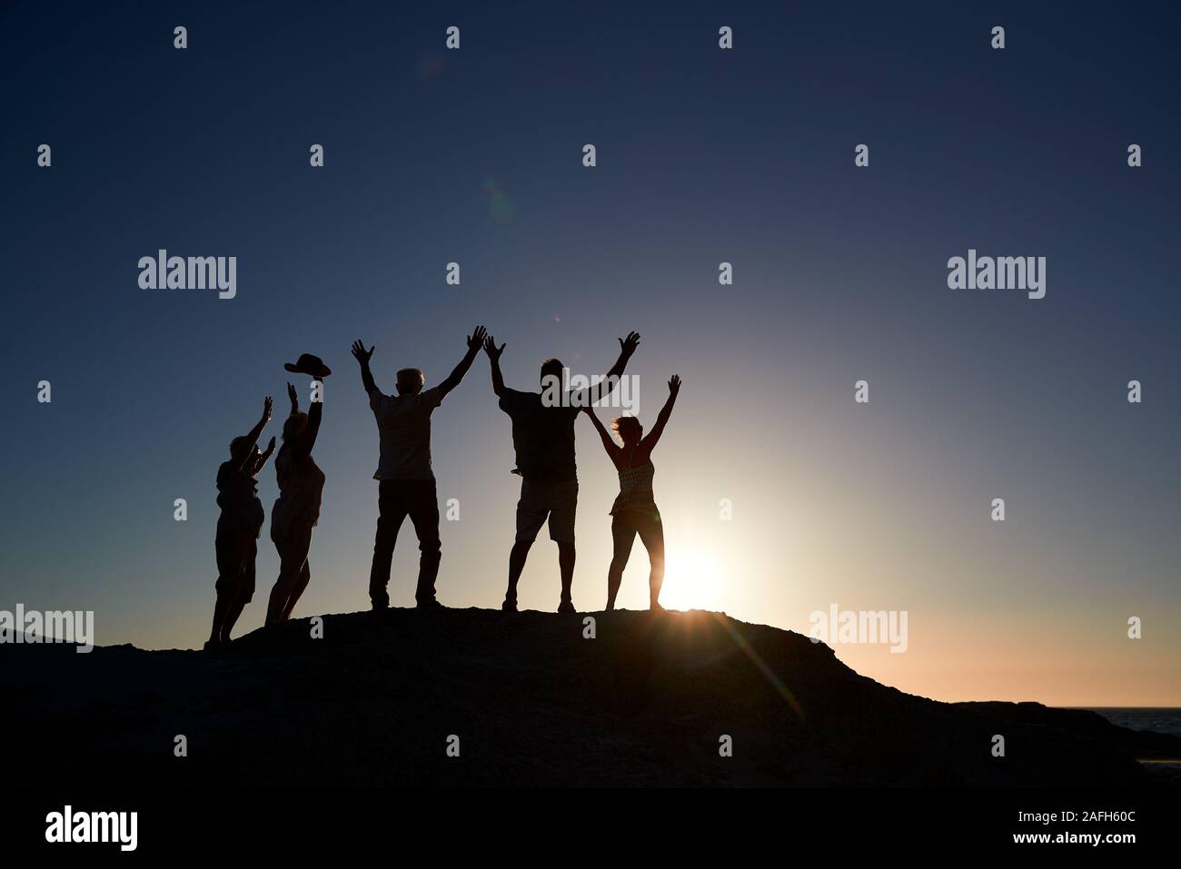 Silhouette der älteren Freunde stehen auf Felsen auf dem Seeweg durch Vermietungen bei Sonnenuntergang mit ausgestreckten Armen Stockfoto