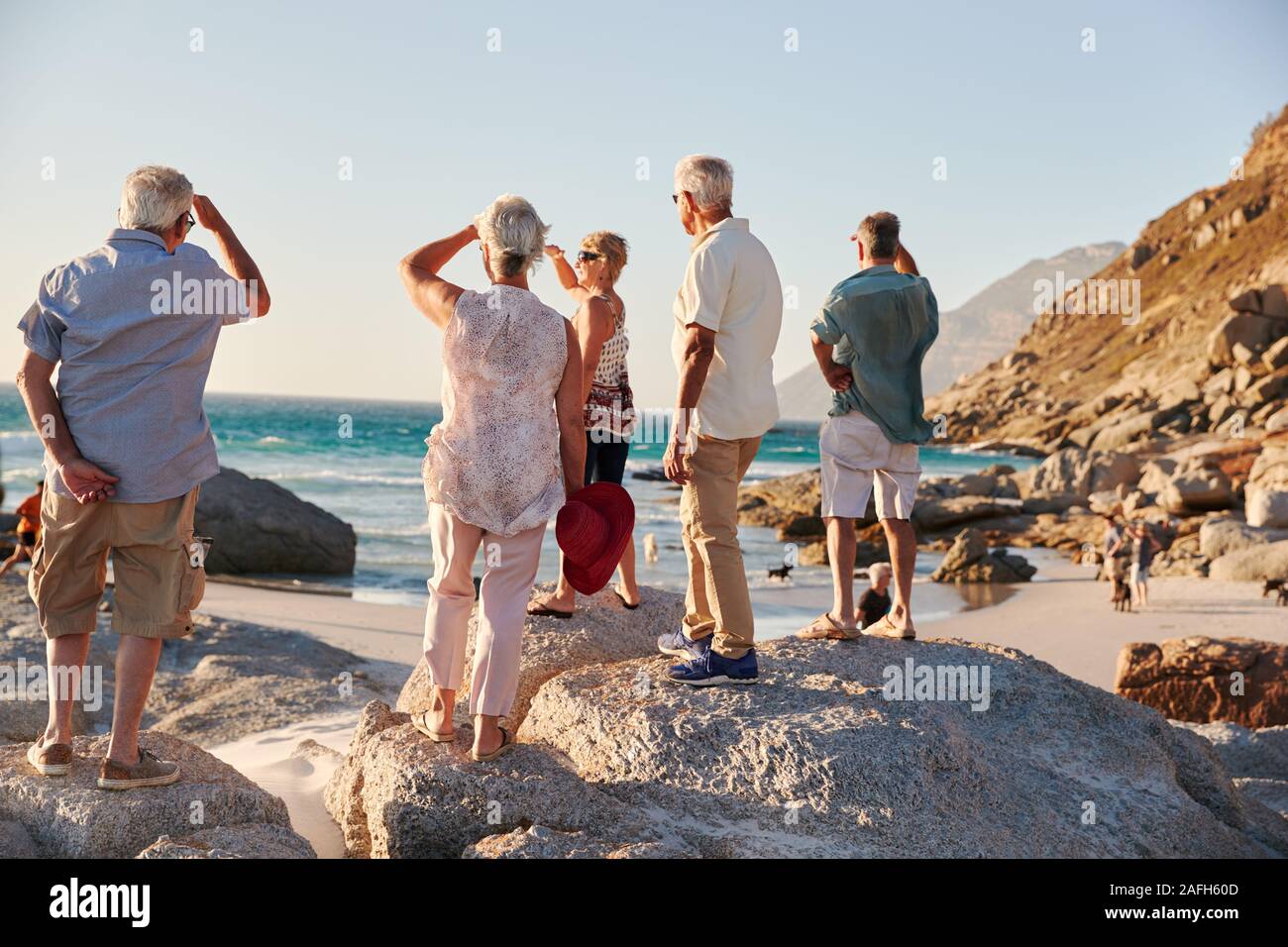 Ansicht der Rückseite des Älteren Freunde stehen auf Felsen auf Sommer Gruppe Ferienhäuser mit Meerblick Stockfoto