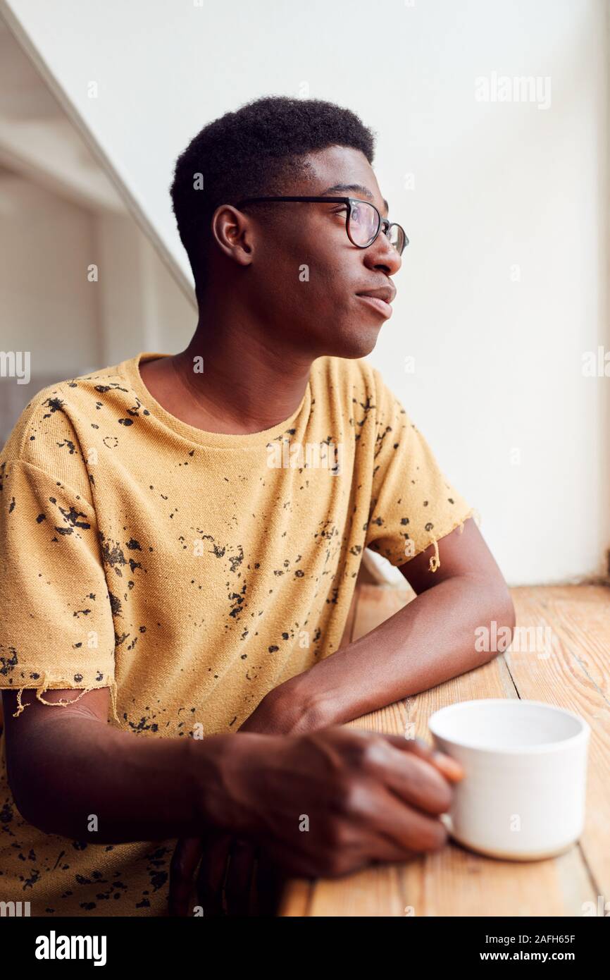 Junge Mann in Loft Apartment Blick Aus Fenster mit heißen Getränken Stockfoto