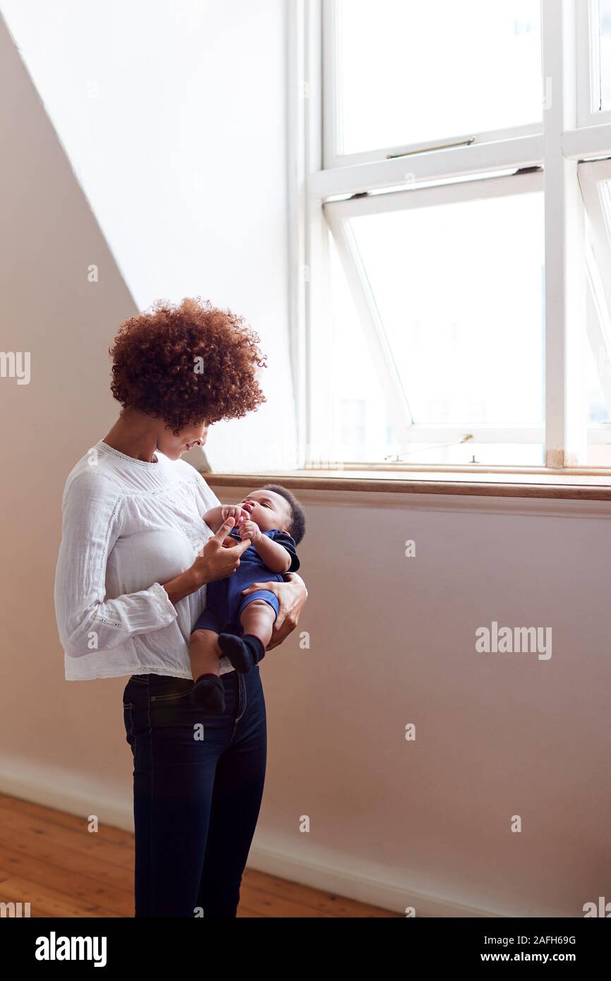 Liebevolle Mutter halten Schlafen Neugeborene durch Fenster in Loft Apartment Stockfoto