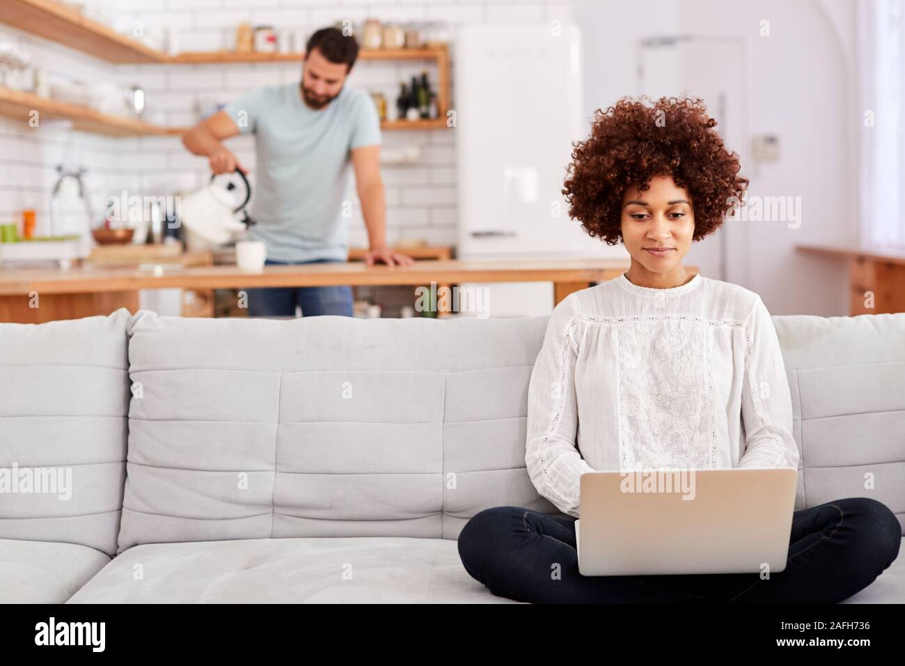 Frau entspannende Sitzen auf einem Sofa zu Hause mit Laptop mit Mann in der Küche Gießen Trinken Stockfoto