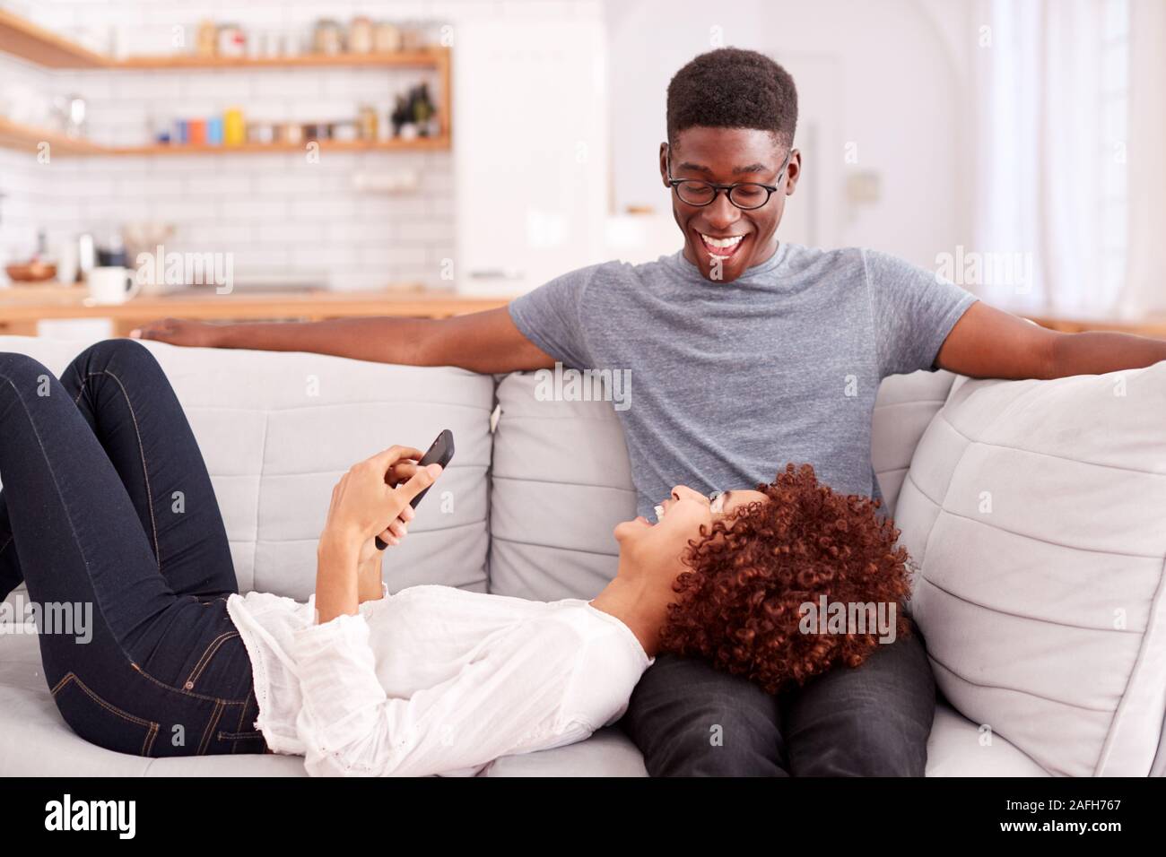 Junges Paar Entspannen auf dem Sofa zu Hause auf Mobiltelefon zusammen Stockfoto