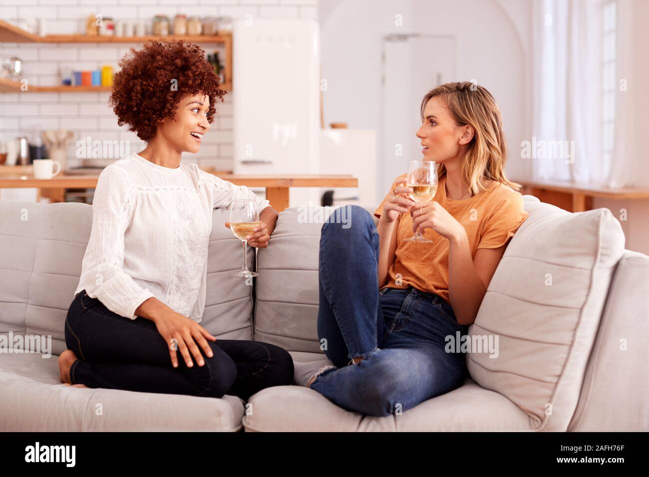 Zwei weibliche Freunde Entspannen auf dem Sofa zu Hause bei einem Glas Wein zusammen gesprochen Stockfoto