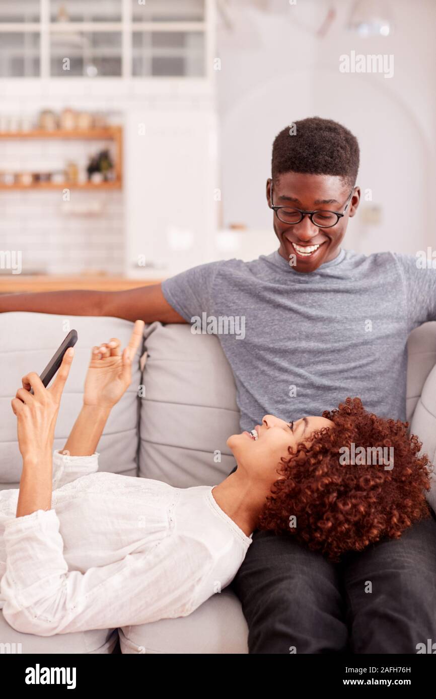 Junges Paar Entspannen auf dem Sofa zu Hause auf Mobiltelefon zusammen Stockfoto