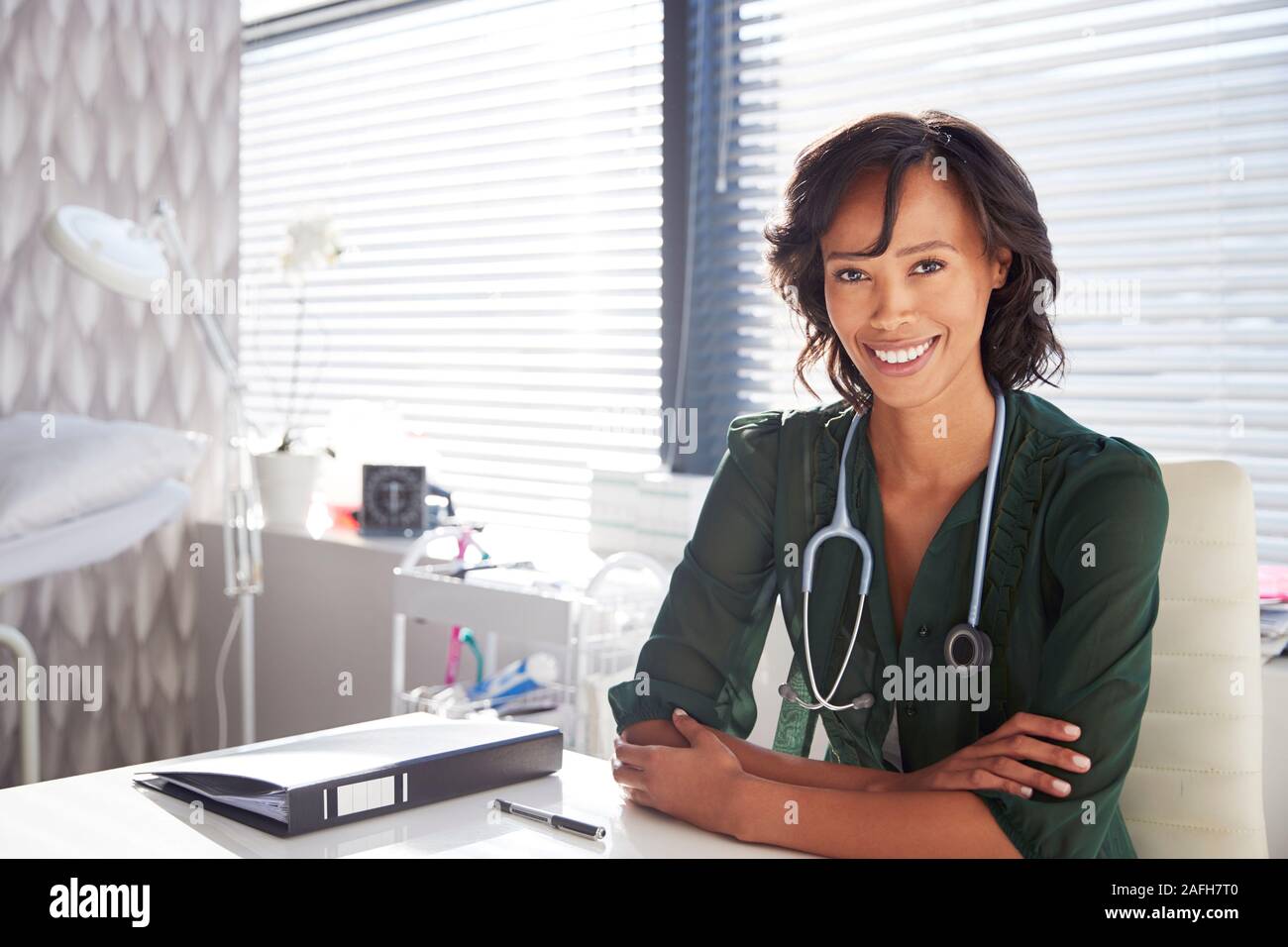 Portrait von lächelnden Frau Doktor mit Stethoskop, hinter einem Schreibtisch im Büro Stockfoto