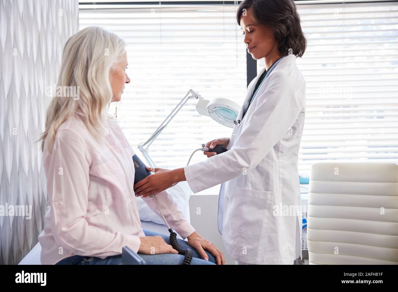 Frau Patient, der Blutdruck durch Ärztin in Office Stockfoto