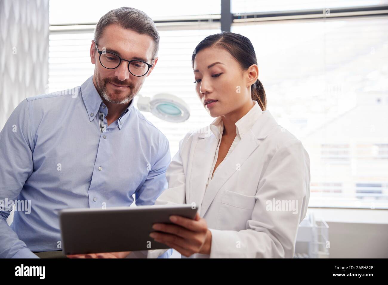 Ärztin Zeige ältere männliche Patienten Testergebnisse auf Digital Tablet im Büro Stockfoto