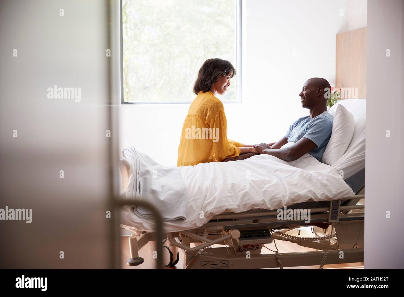 Frau besuchen und im Gespräch mit Patienten Mann im Krankenhaus Bed Stockfoto