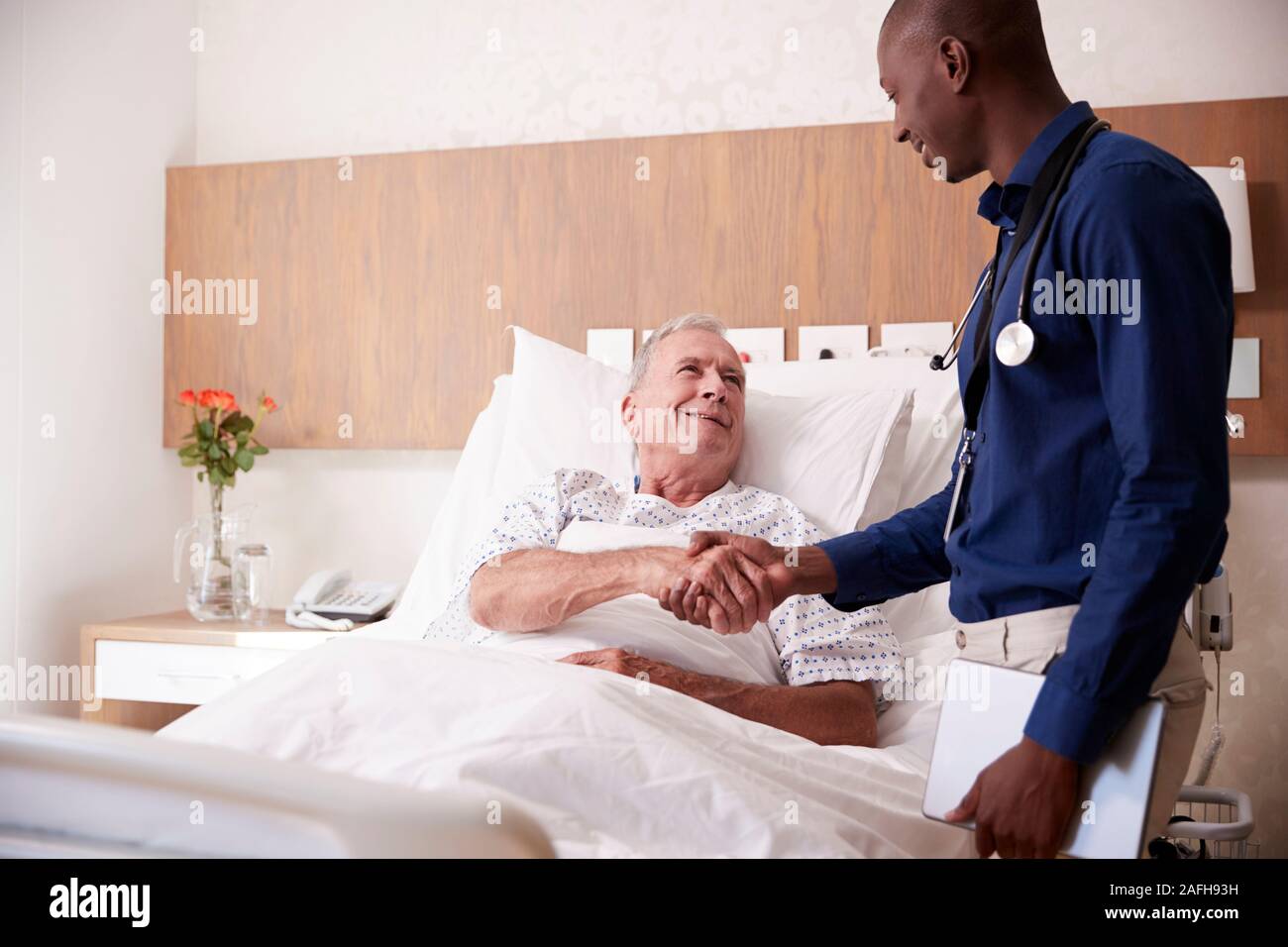 Arzt Händeschütteln mit älteren männlichen Patienten im Krankenhausbett in Geriatrische Einheit Stockfoto