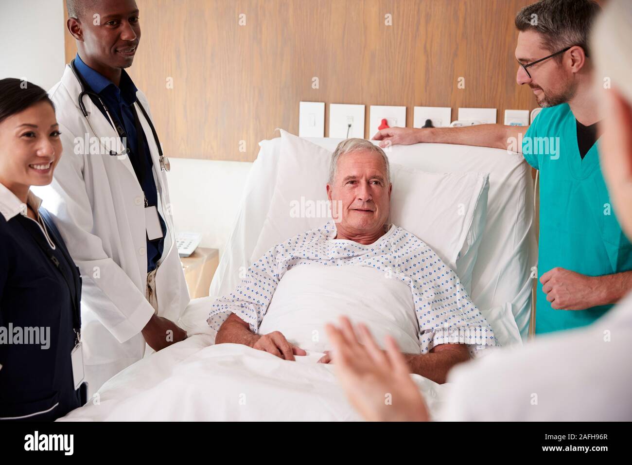 Medizinisches Team auf Runden Treffen rund um Bett der älteren männlichen Patienten Stockfoto