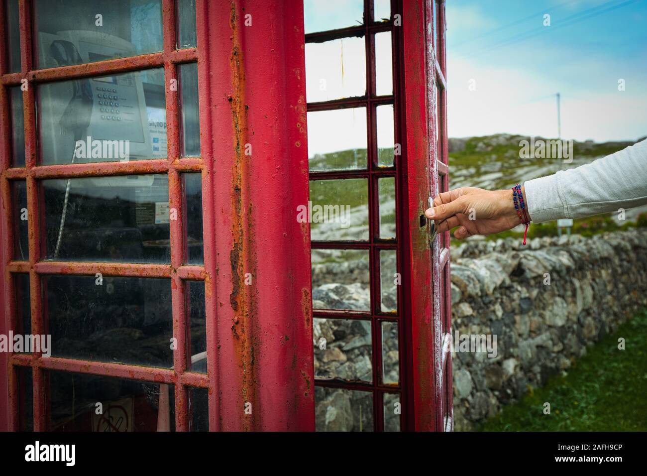 Die Hand von Mans öffnet Tür zu der traditionellen roten Fernsprechbox auf der Insel Harris, Outer Hebrides, Schottland Stockfoto