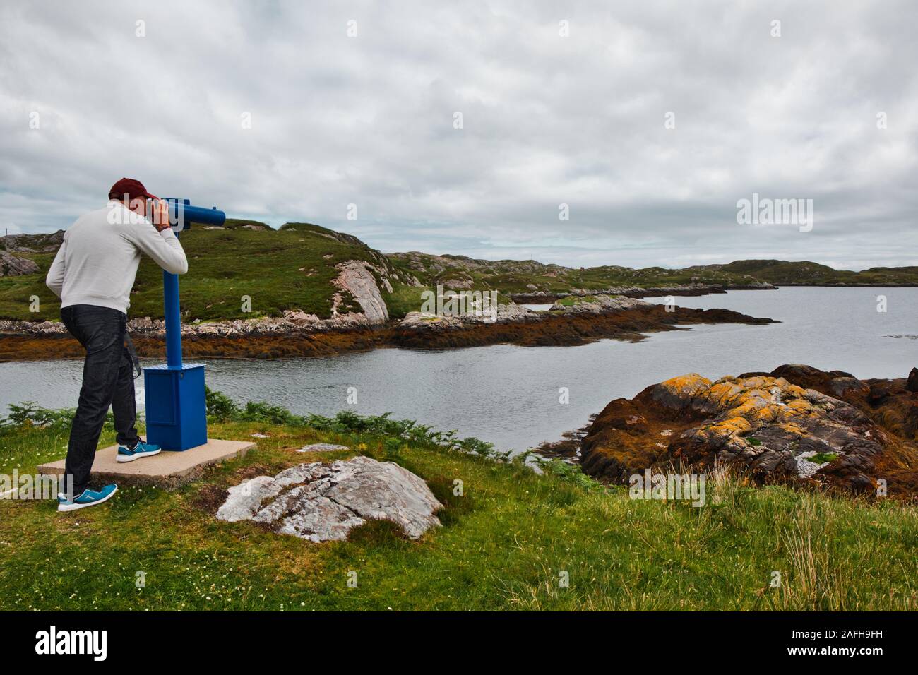 Mann mittleren Alters, der durch das Teleskop an der Atlantikküste von Insel Harris, Outer Hebrides, Schottland, blickt Stockfoto