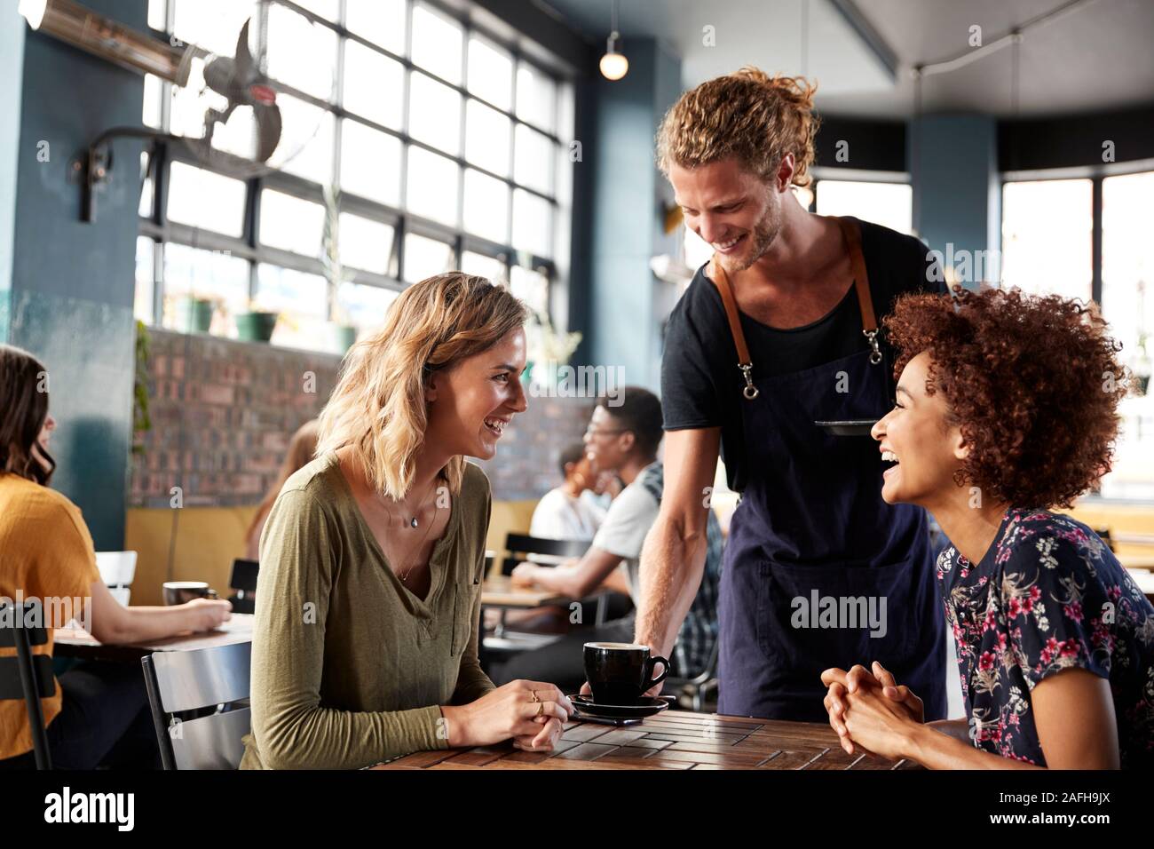 Zwei weibliche Freunde am Tisch sitzen in Coffee Shop serviert der Kellner Stockfoto