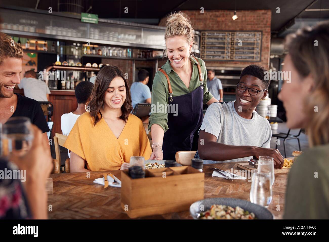 Kellnerin serviert Gruppe junger Freunde treffen für Getränke und Essen im Restaurant Stockfoto