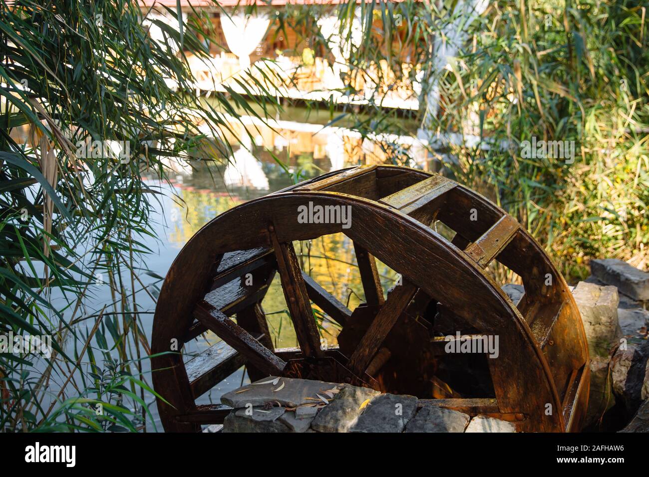 Das alte Wasserrad ist auf dem See von Bäumen und Felsen an einem sonnigen Tag umgeben. Stockfoto