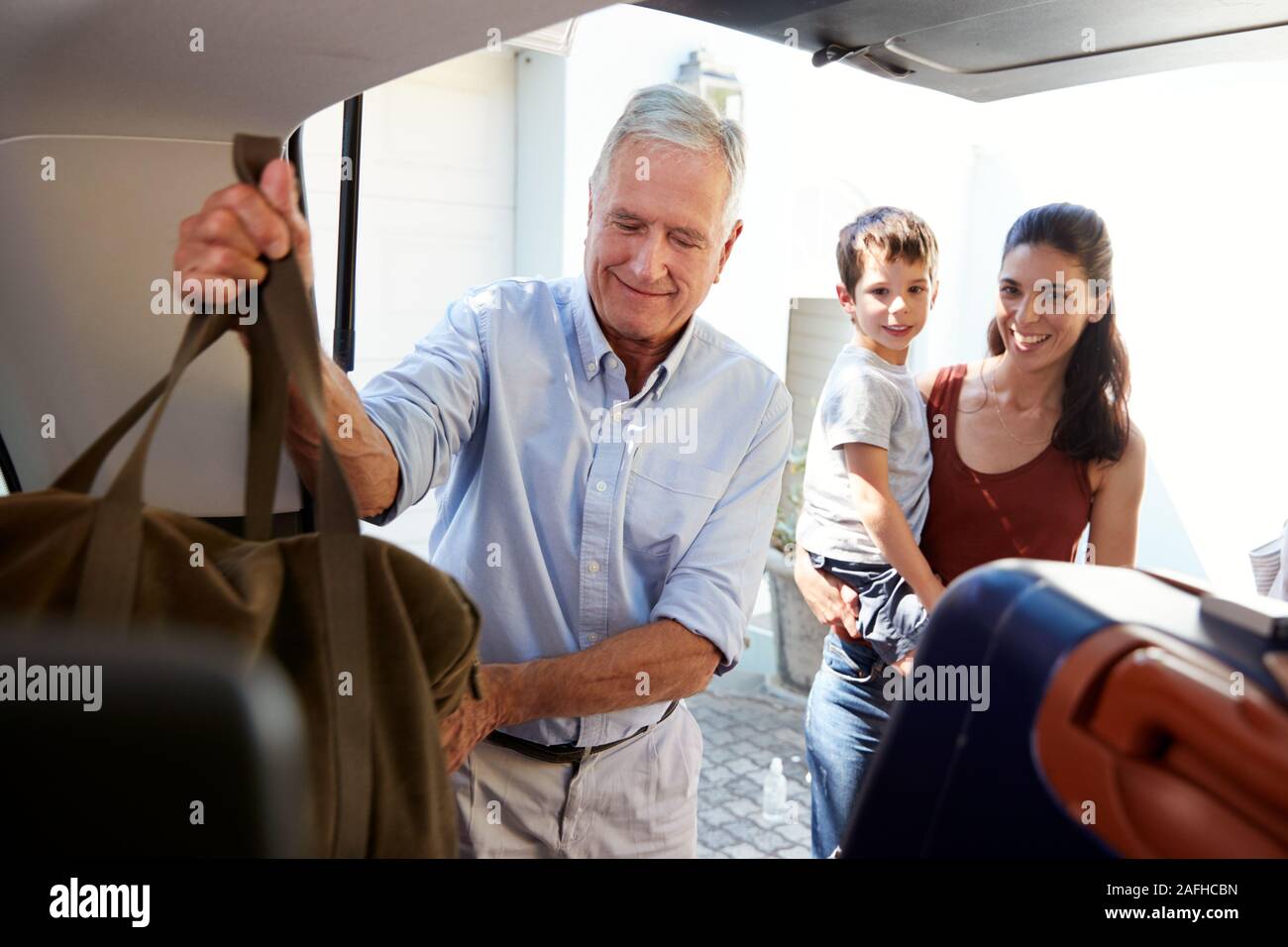 Senior weiße Mann Verpackung Kofferraum mit Urlaubsgepäck, durch seine erwachsene Tochter und Enkel beobachtet Stockfoto