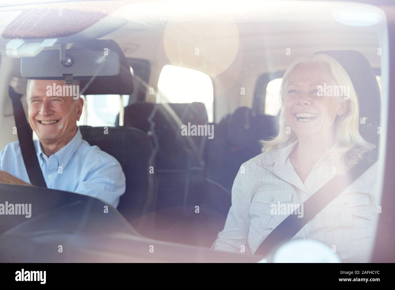 Senior weiß Paar fahren in ihr Auto an einem sonnigen Tag, durch die vordere Windschutzscheibe Stockfoto