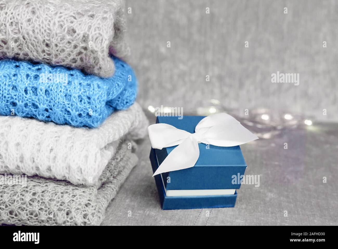 Stilvolle gestrickt, pastellfarbenen Pullover im Stapel und trendigen blau  gefärbten vorhanden Feld mit weißem satin schleife auf Samtigen Stoff  Hintergrund gefaltet. Winter Stockfotografie - Alamy