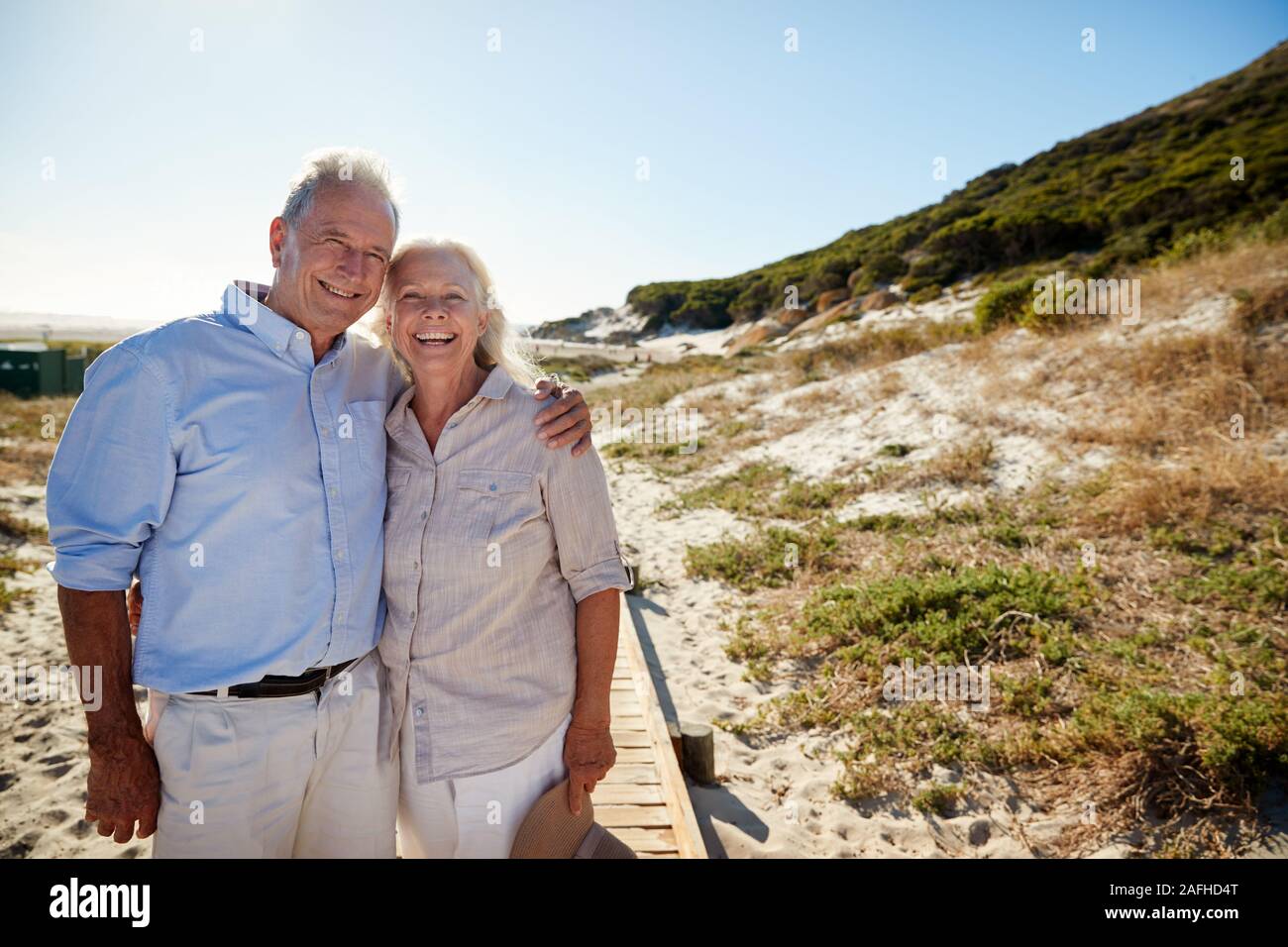 Senior weiß Paar stehend auf einem Strand umarmen und lächelnd auf Kamera, drei Viertel Länge Stockfoto