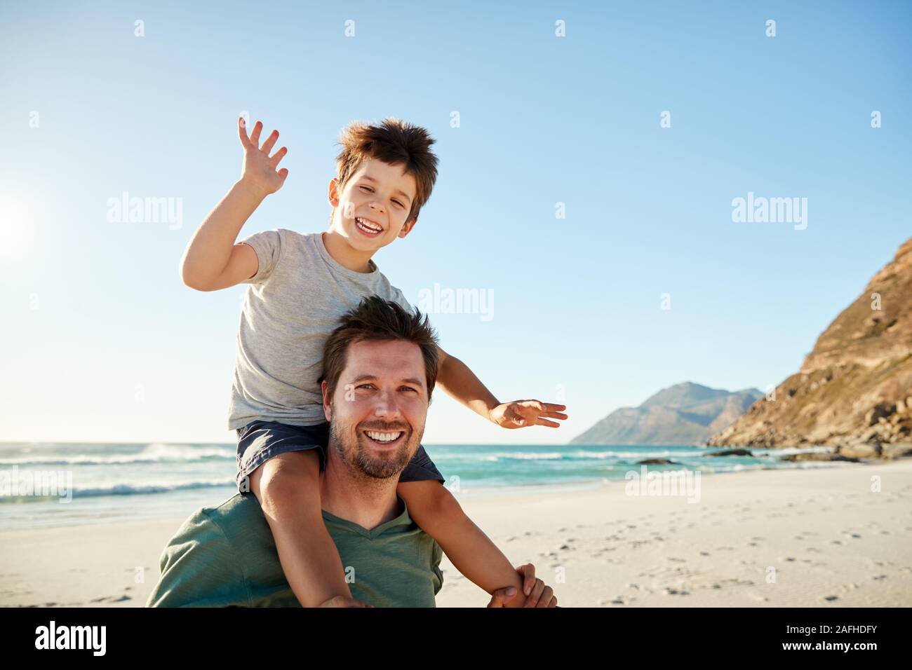 Mitte nach weißen Mann auf einem Strand, seinen vier Jahre alten Sohn sitzen auf den Schultern winken, Nahaufnahme Stockfoto