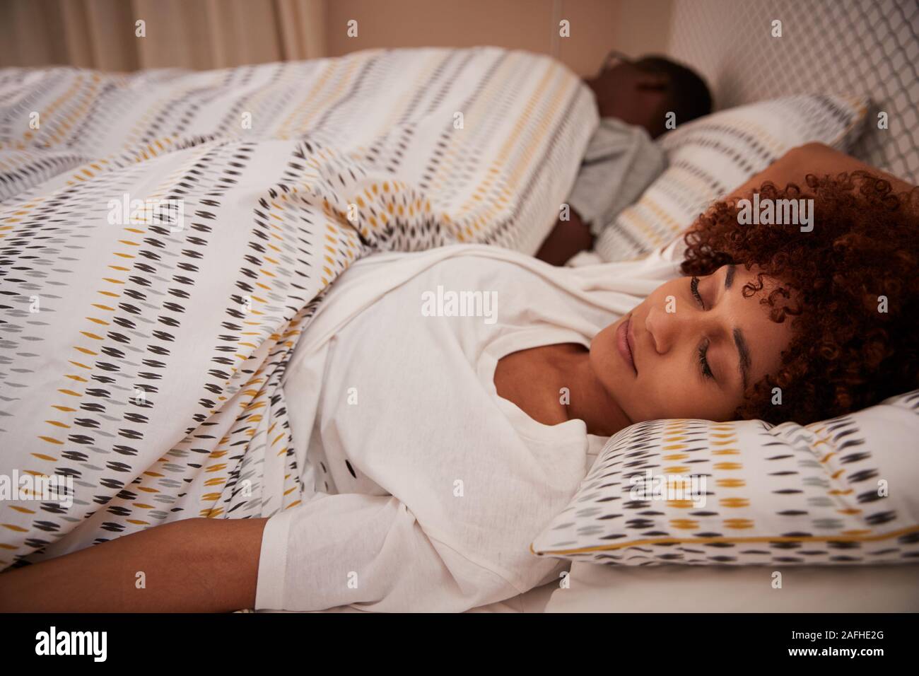 Tausendjährigen afrikanischen amerikanischen liegende Frau auf dem Rücken schläft im Bett, Ihr Partner im Hintergrund Stockfoto