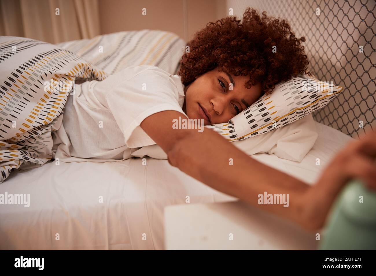 Tausendjährige afrikanische amerikanische Frau halb schlafend im Bett, Wecker zu stoppen, in der Nähe Stockfoto