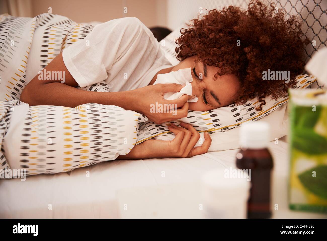 Tausendjährige afrikanische amerikanische Frau im Bett lag, Blasen, ihre Nase in ein Papiertaschentuch, Seitenansicht, in der Nähe Stockfoto