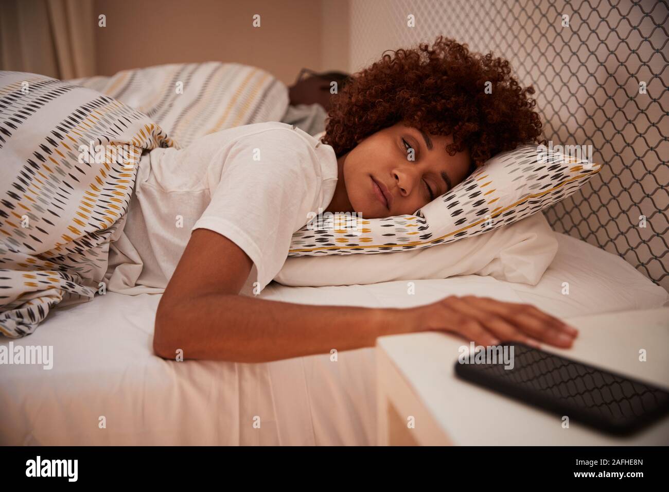 Tausendjährige afrikanische amerikanische Frau halb schlafend im Bett, für Ihr Smartphone, in der Nähe Stockfoto