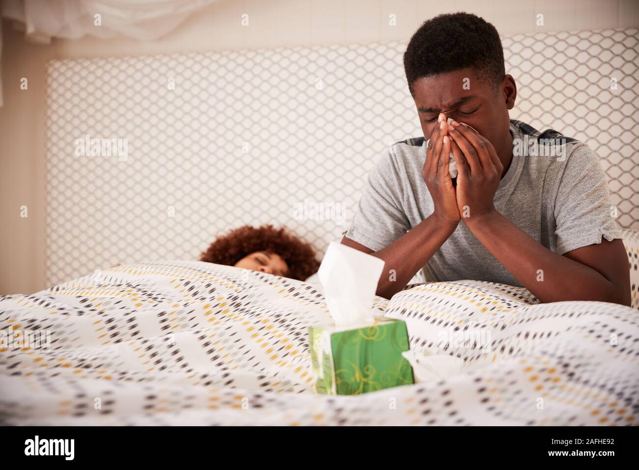 Tausendjährigen afrikanischen amerikanischen Mann im Bett sitzend blasen Nase, während sein Partner schläft, in der Nähe Stockfoto