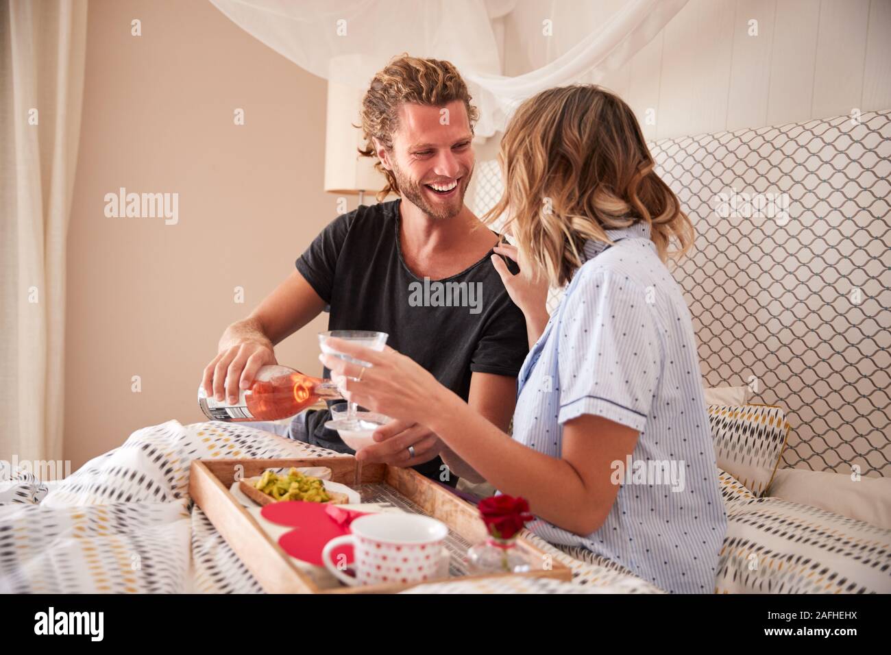 Tausendjährige weiß Paar feiern mit Champagner, Frühstück und Geschenke im Bett, in der Nähe Stockfoto