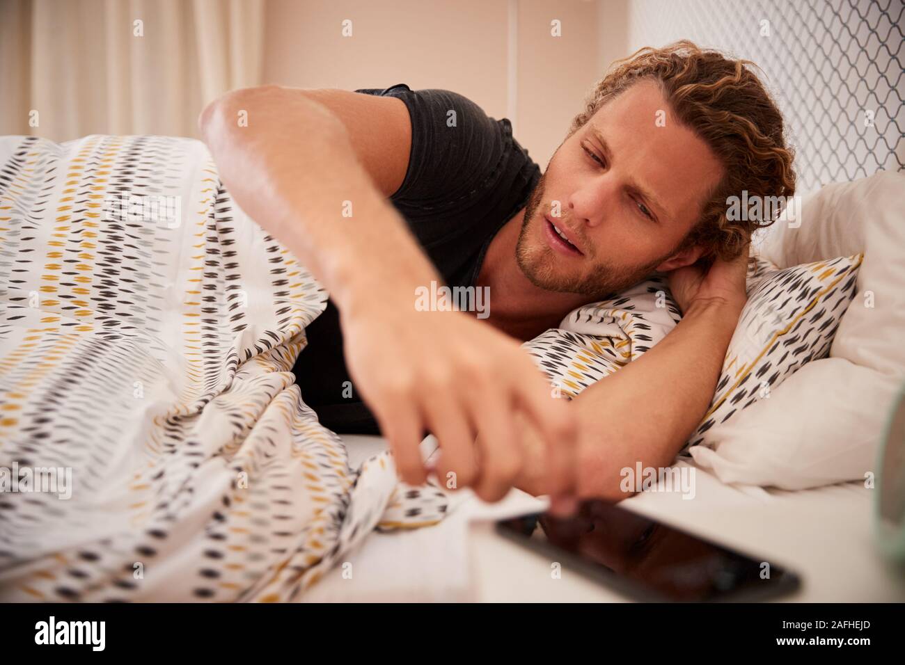 Tausendjährige weiße Mann Aufwachen in schlecht und erreichen für Smartphone, in der Nähe Stockfoto