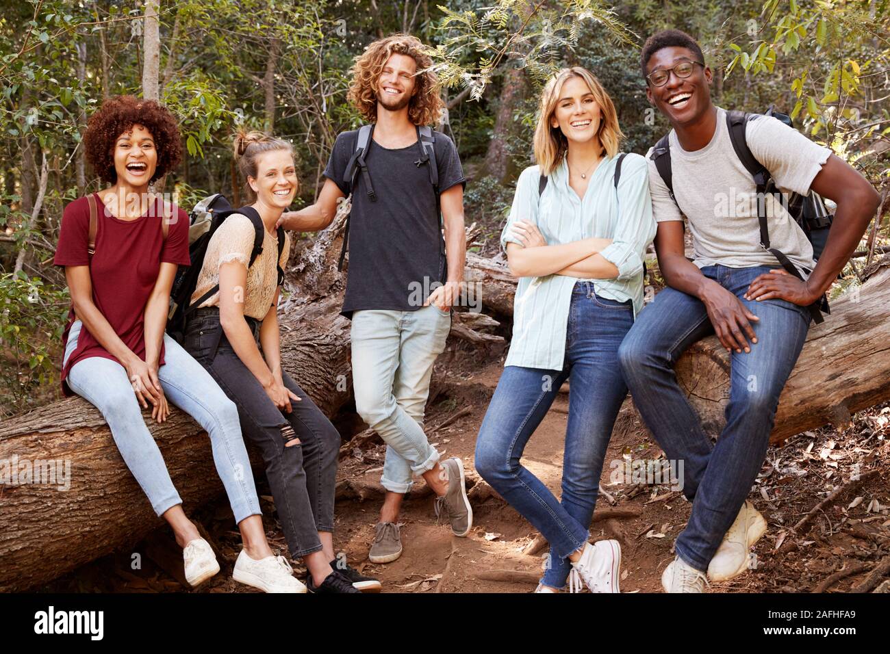 Junge Erwachsene Freunde wandern im Wald auf einem Baum, lächelnd in die Kamera, volle Länge Stockfoto