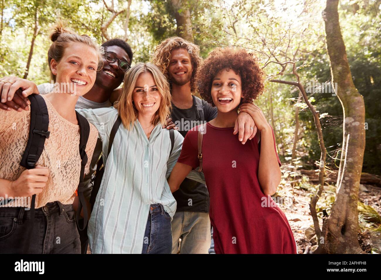 Fünf junge erwachsene Freunde wandern in einem Wald lächelnd in die Kamera, drei Viertel Länge, in der Nähe Stockfoto