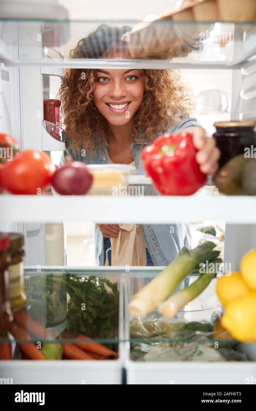Blick aus dem Inneren der Kühlschrank als Frau öffnet Tür und Entpackt Shopping Bag von Lebensmitteln suchen Stockfoto