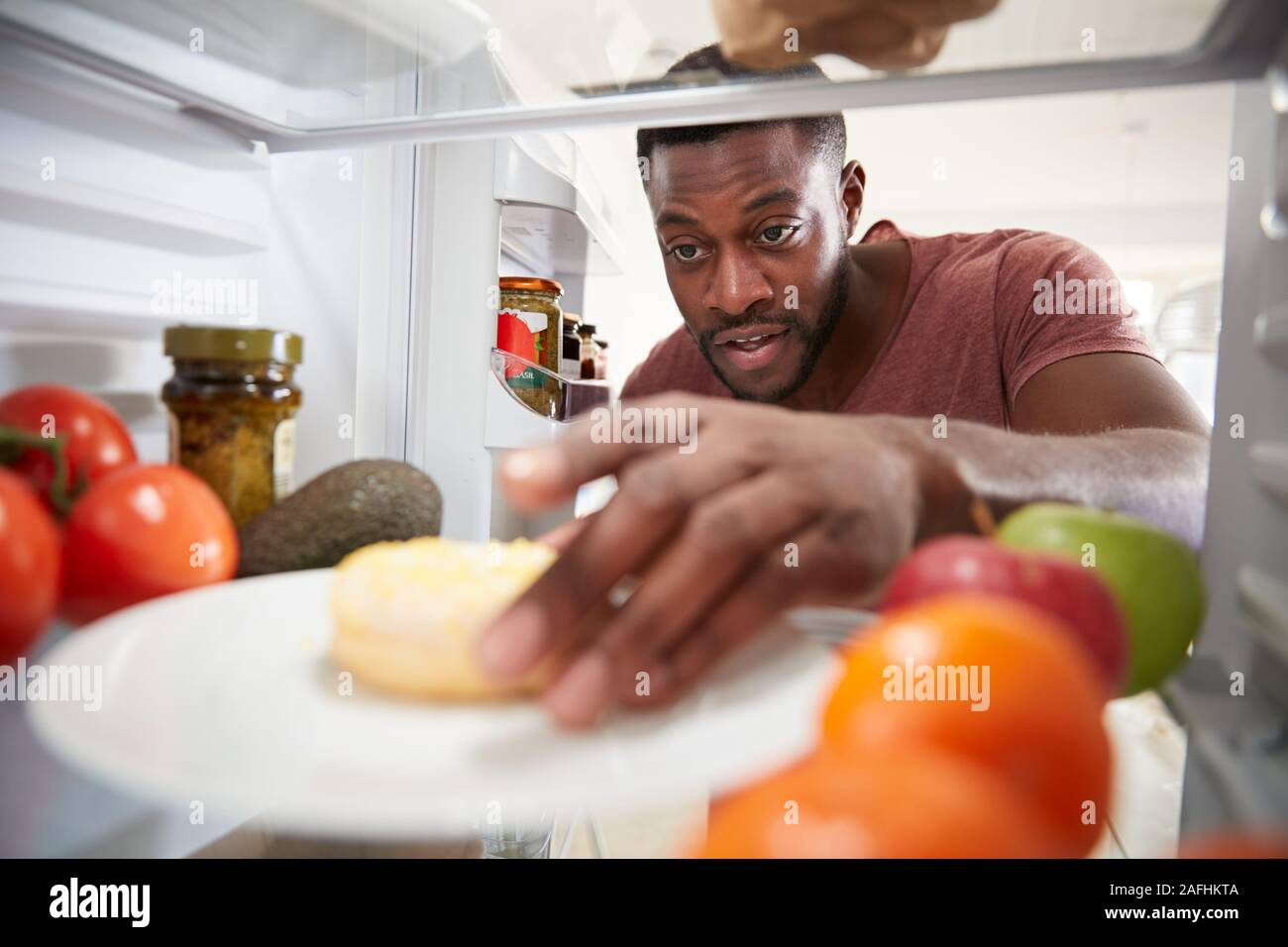 Blick aus dem Inneren des Kühlschranks als Mensch öffnet Tür und erreicht für ungesunde Donut Suchen Stockfoto