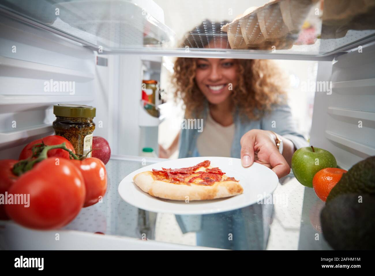 Anzeigen, die von der Innenseite der Kühlschrank als Frau öffnet Tür für Übrig gebliebene Takeaway Pizza Stockfoto