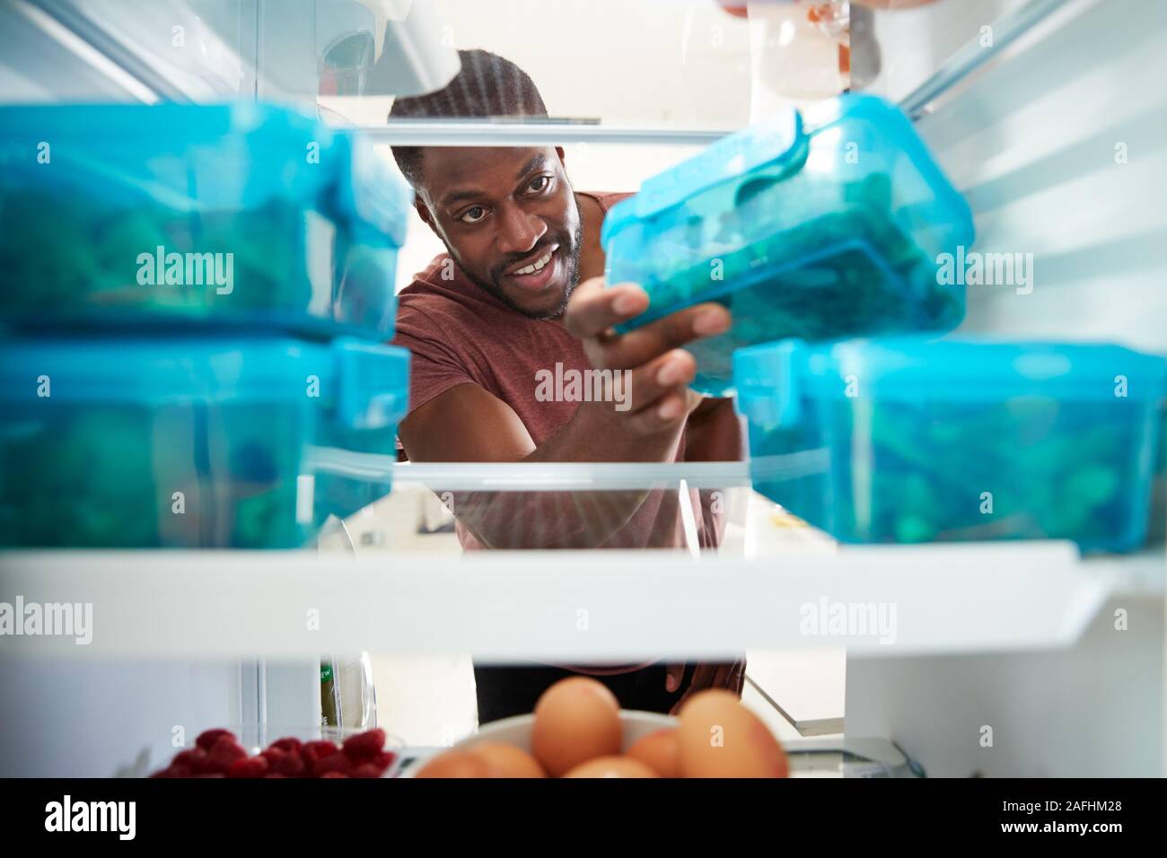 Blick aus dem Inneren der Kühlschrank als Mann, Nimmt gesundes Lunchpaket in Container Stockfoto