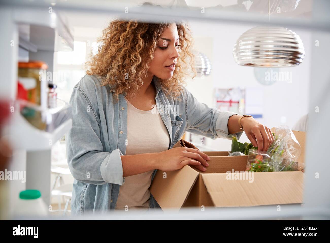 Blick aus dem Inneren des Kühlschranks als Frau entpackt Online Home Food Delivery Suchen Stockfoto