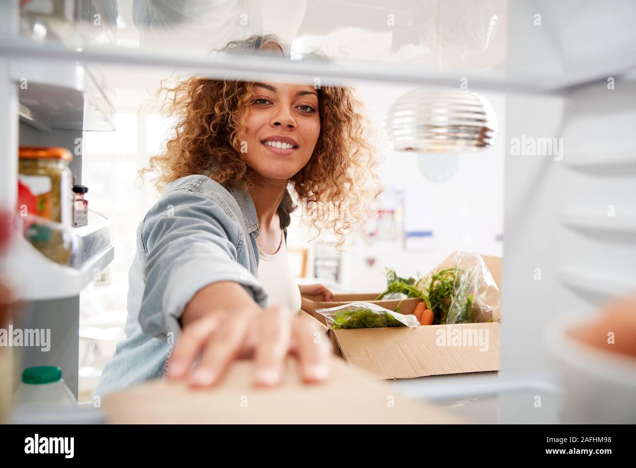 Blick aus dem Inneren des Kühlschranks als Frau entpackt Online Home Food Delivery Suchen Stockfoto