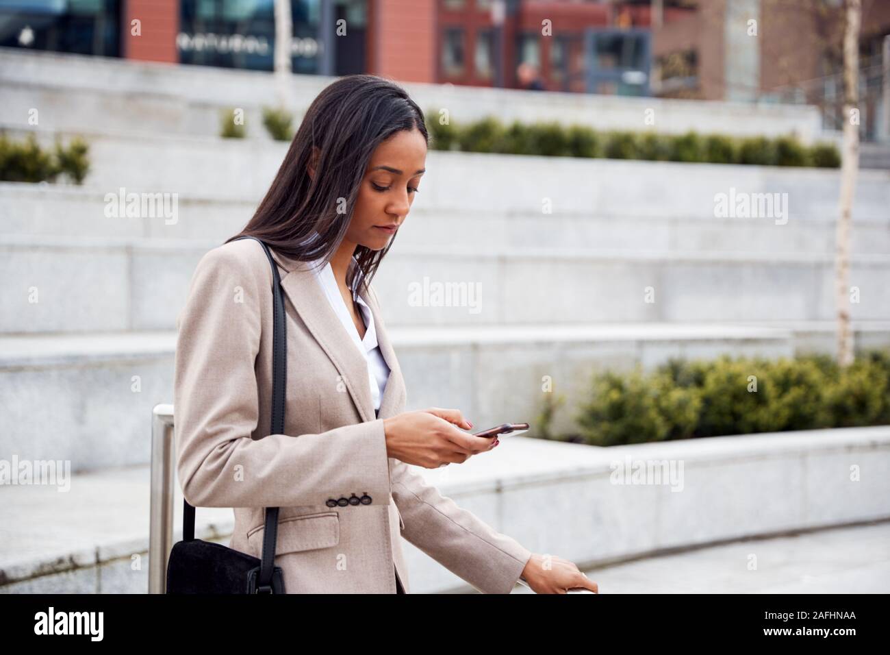 Geschäftsfrau Pendeln zum Arbeitsplatz Abrufen von Nachrichten auf dem Handy außerhalb Modernes Bürogebäude Stockfoto