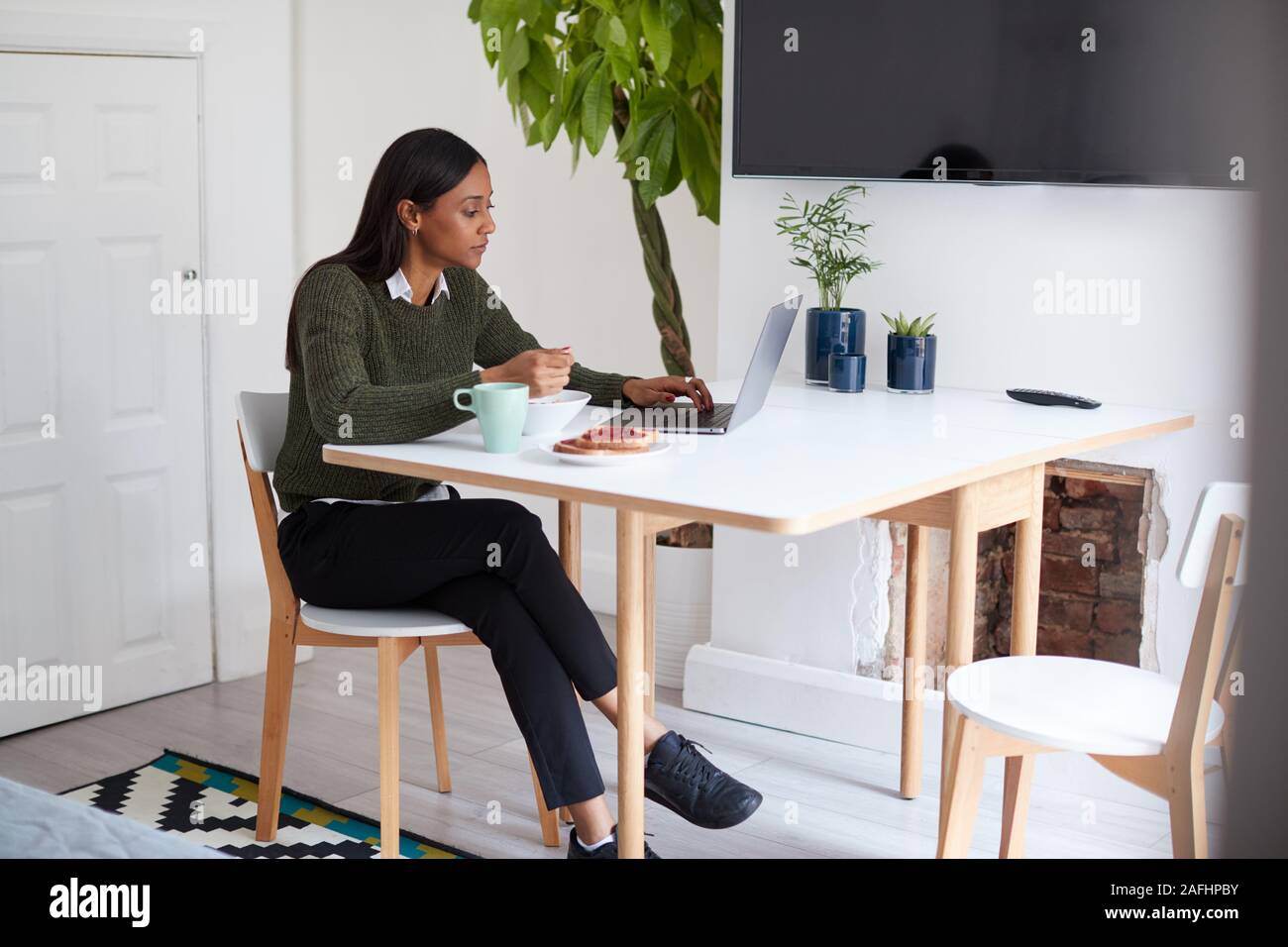 Geschäftsfrau zu Hause essen Frühstück in der Laptop suchen, bevor sie für Arbeit Stockfoto