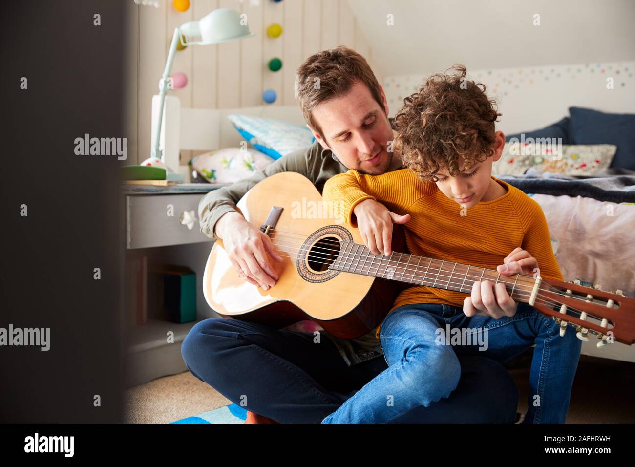 Einzelnen Vater zu Hause mit Sohn lehrte ihn zu spielen akustische Gitarre im Schlafzimmer Stockfoto
