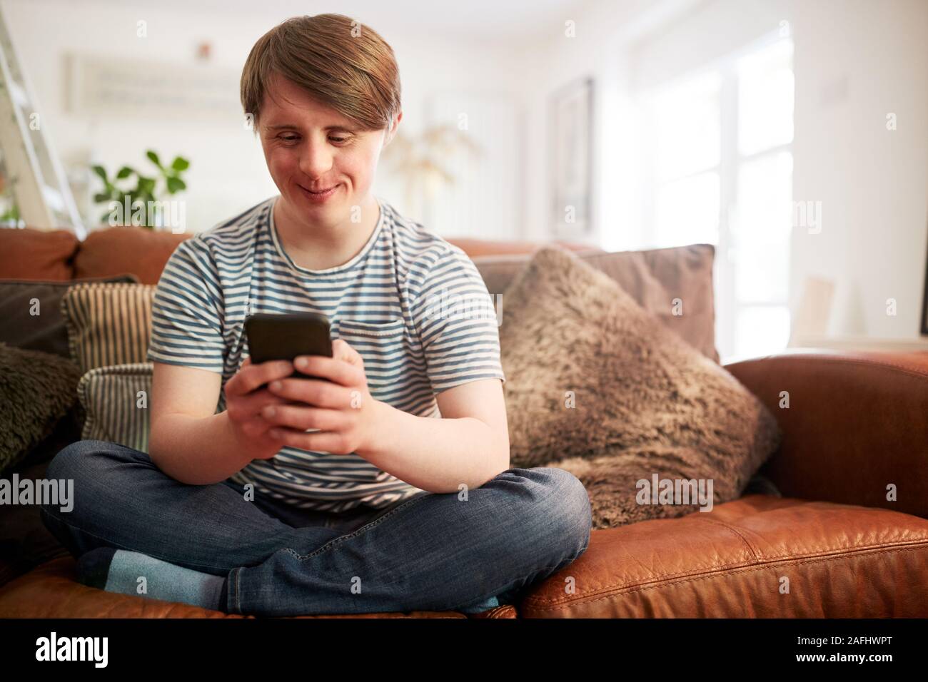 Junge Abstiegsyndrom Mann sitzt auf einem Sofa mit Handy zu Hause Stockfoto