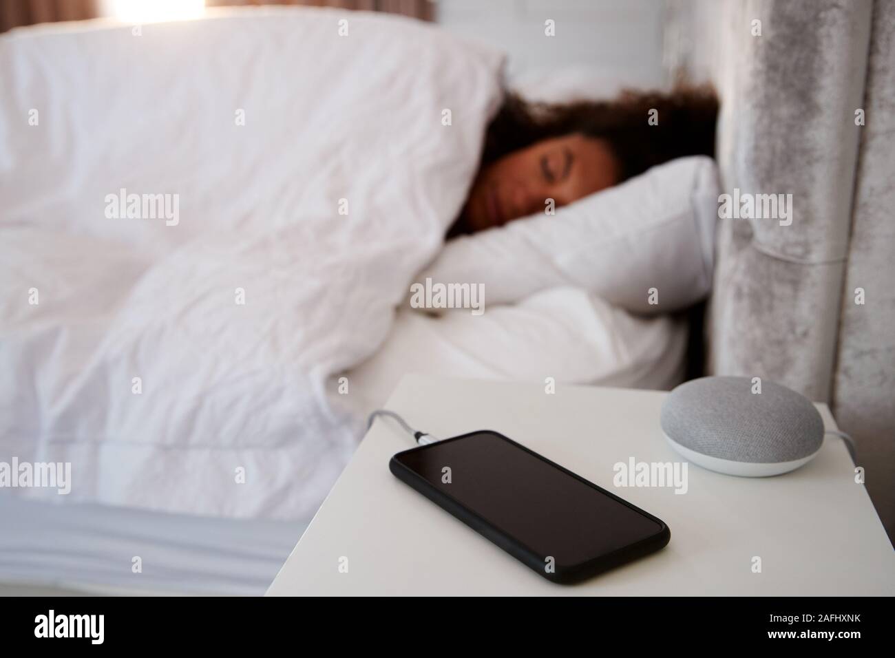 Frau schlafend im Bett mit Handy und Voice Assistant auf dem Nachttisch Stockfoto