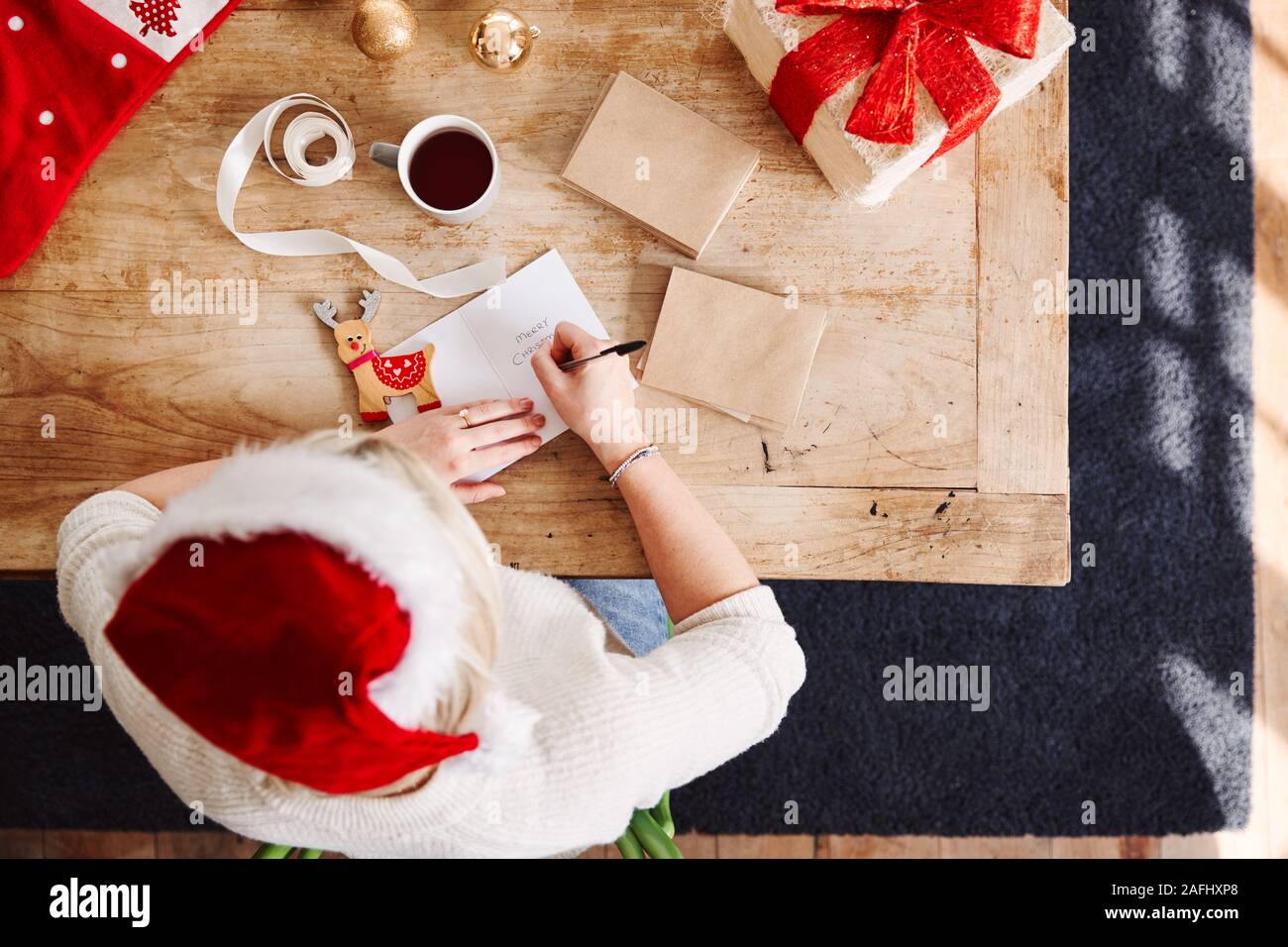 Overhead Shot Suchen auf Frau schreiben In Weihnachtskarte und Verpackung Geschenk tragen Santa Hut Stockfoto
