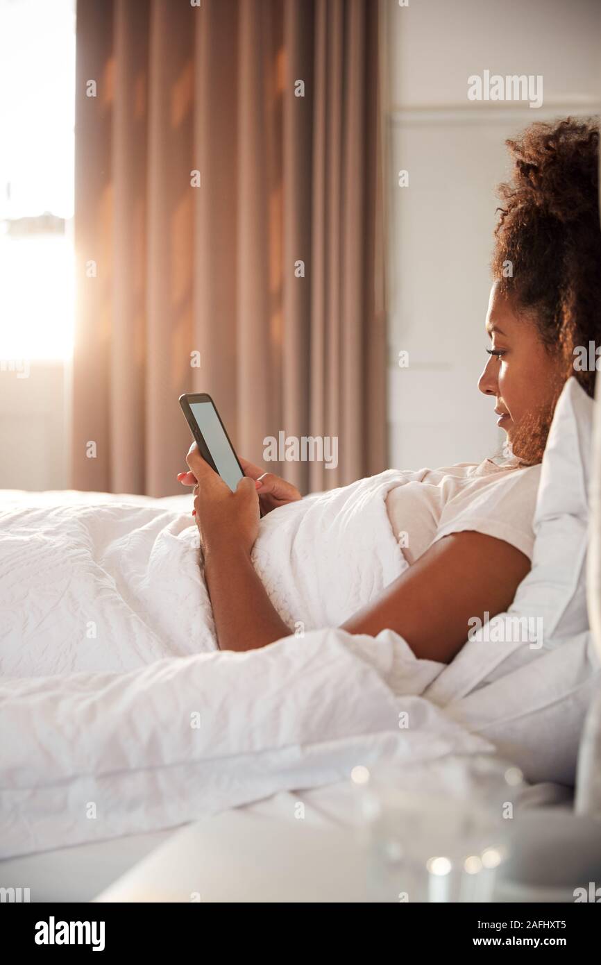 Frau sitzt oben im Bett am Handy suchen, nachdem sie aufgewacht Stockfoto